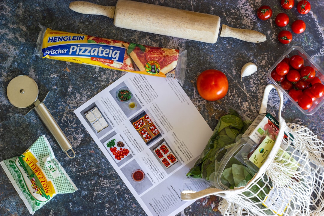 Flat lay of pizza-making ingredients with fresh dough, mozzarella, tomatoes, spinach, garlic, and a recipe guide on a kitchen countertop