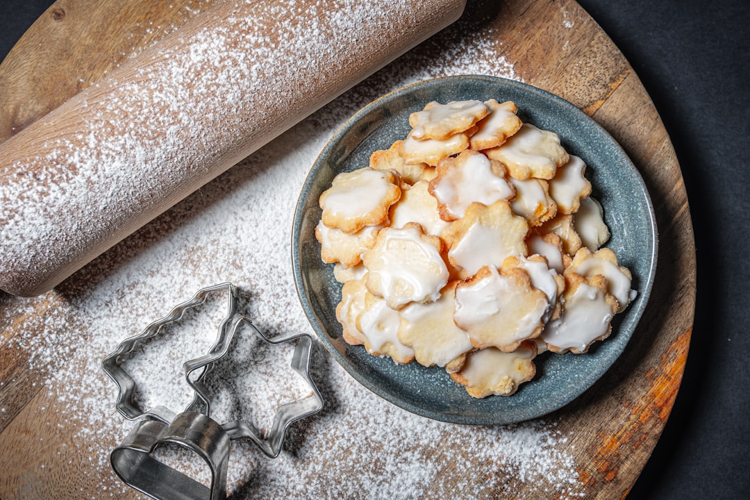 ookies (Center Right): A dark blue-grey, textured ceramic plate holds a stack of small, star or flower-shaped cookies.  The cookies are light brown with slightly burnt edges and are generously topped with a white sugar glaze or royal icing.