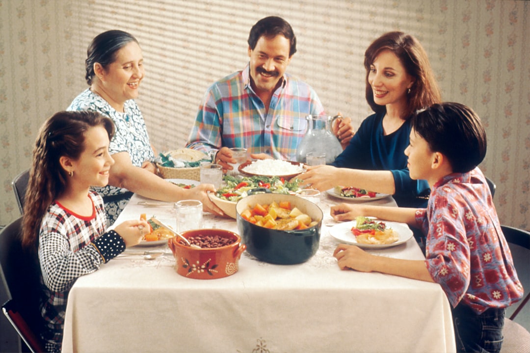 A happy family enjoying a homemade meal together at the dining table, sharing dishes of salad, rice, and vegetables in a warm, cozy home setting.