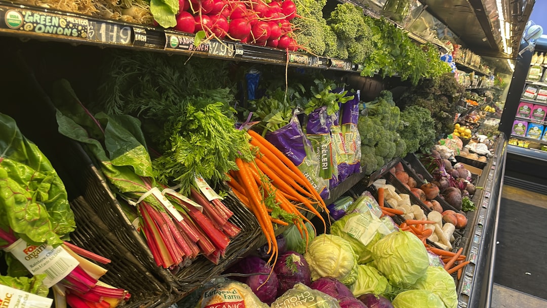 **Alt text:** Fresh produce display in a grocery store with colorful vegetables including carrots, radishes, cabbage, broccoli, and leafy greens neatly arranged on shelves.