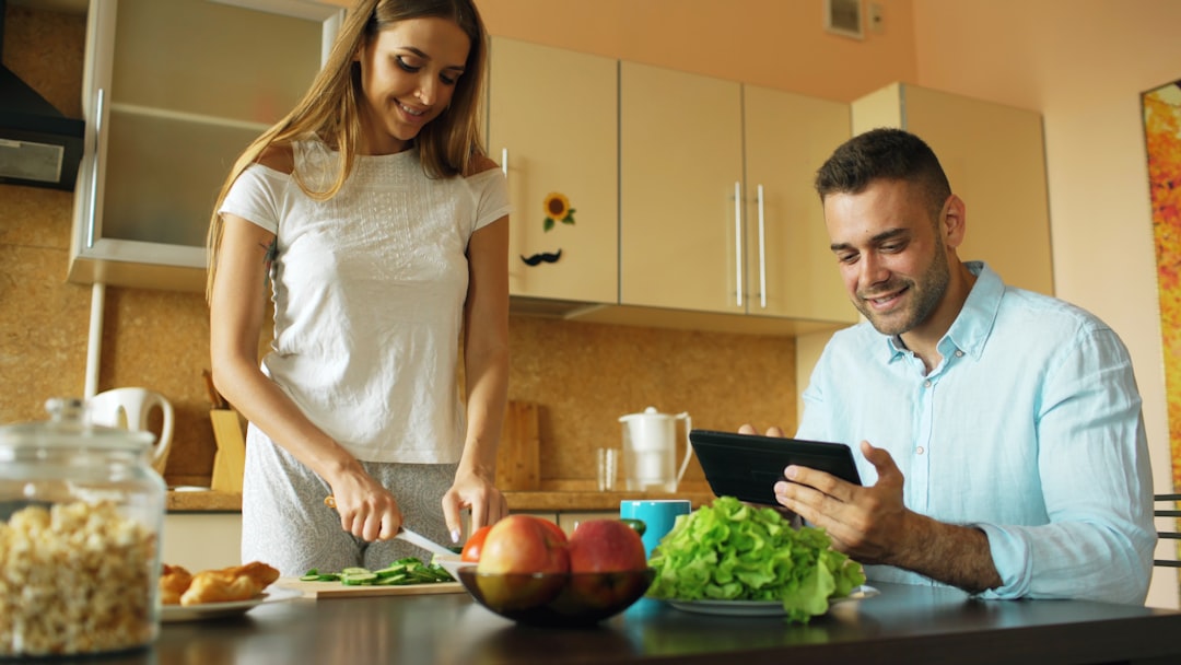 "Smiling couple preparing healthy meal together in modern kitchen while using a digital tablet."
